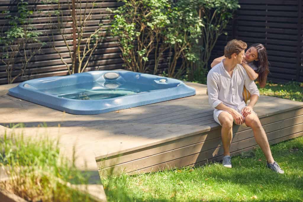 Hot tub installed on a wooden deck surrounded by lush landscaping.